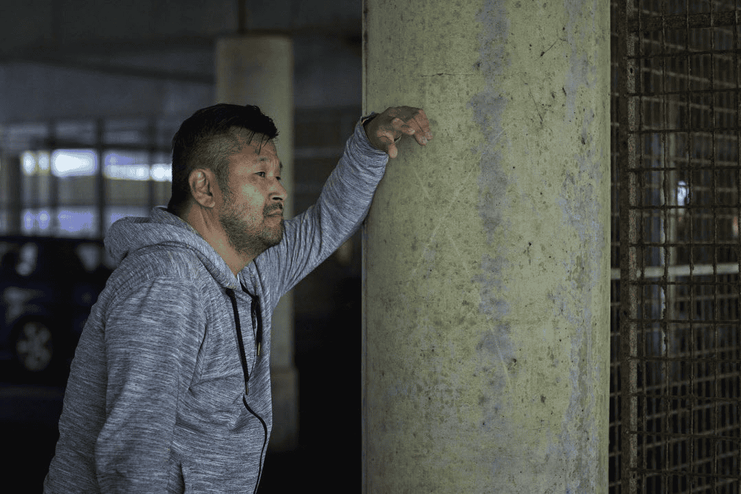 Man in a sweatshirt leaning on an underground pole